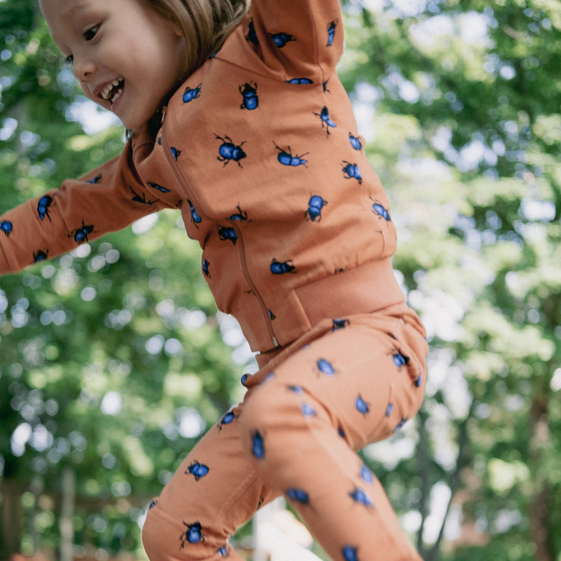 Child jumping from a rock wearing the beetles bomber zip up cardigan in orange with blue beetles.