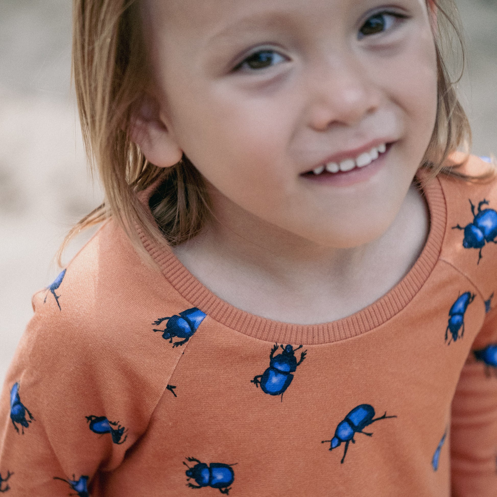 Child wearing an orange tunic with beetles on. Detail of the neckline.