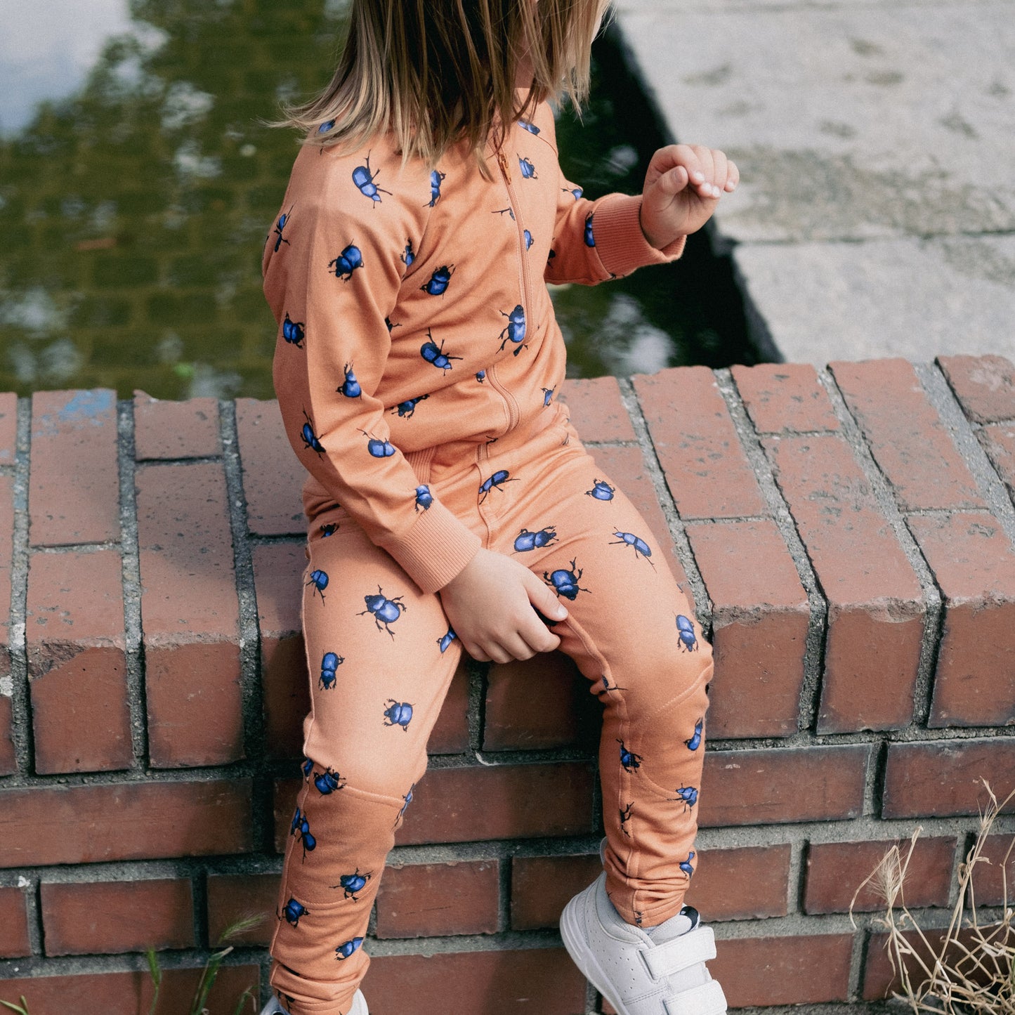 Child sitting on a brick wall wearing the beetle's collection treggings and bomber jacker