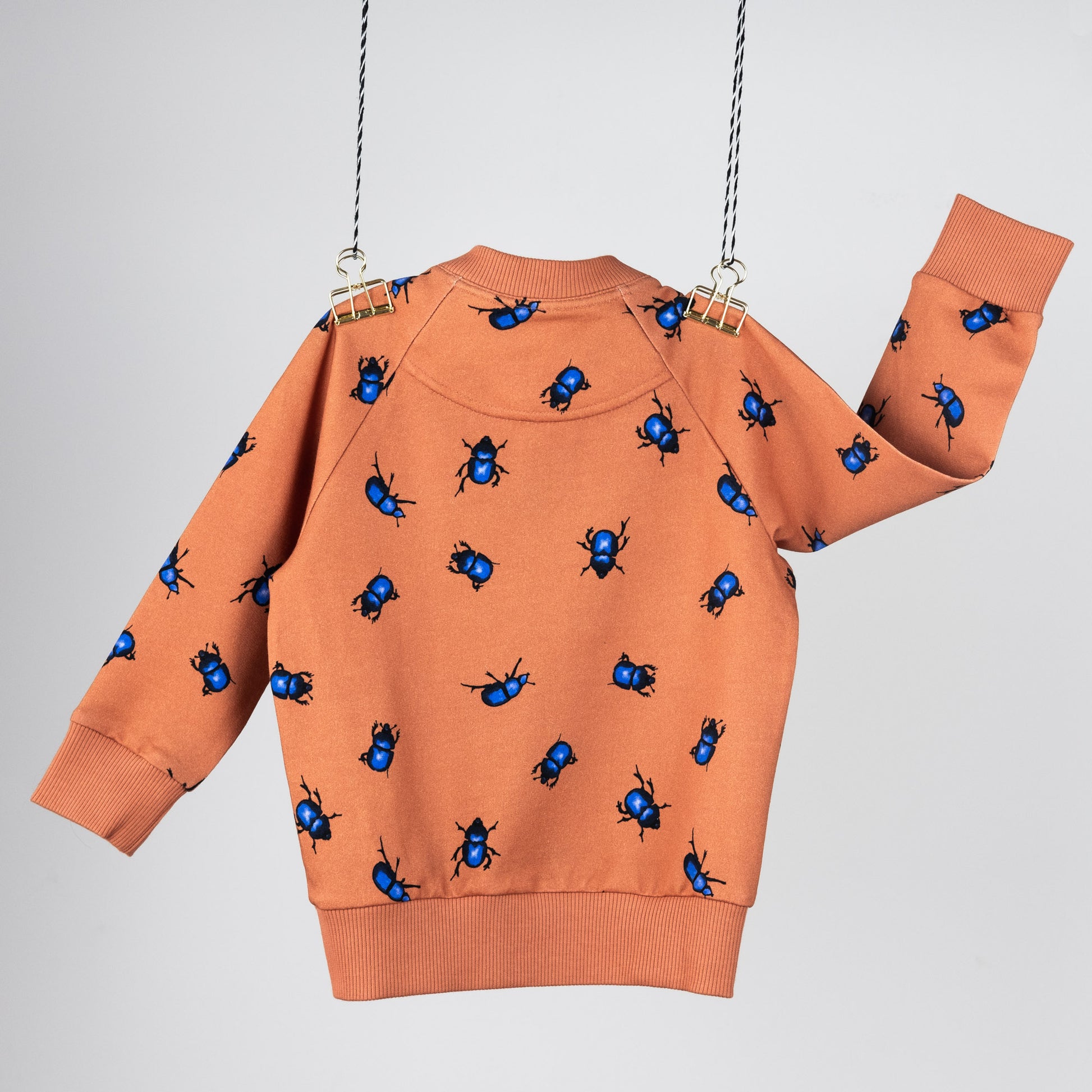 Back view of the bomber jacket. Hanging in front of a light gray background. The jacket is orange with blue beetles.