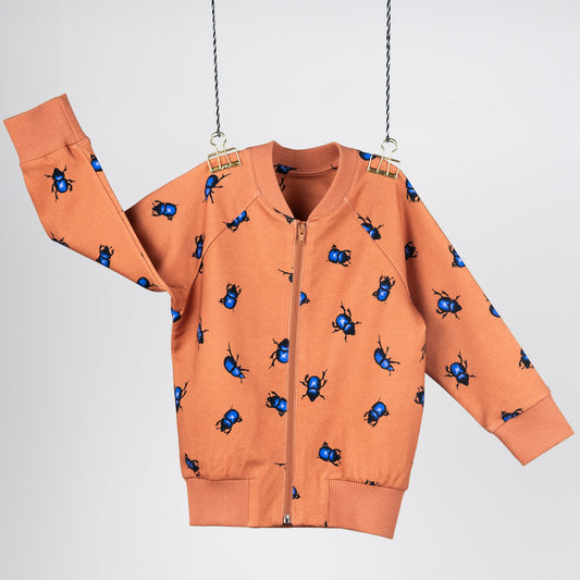 Front view of the bomber jacket. Hanging in front of a light gray background. The cardigan is orange with blue beetles.