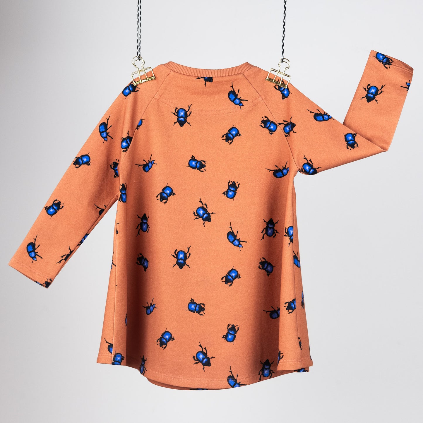 Back view of the Beetle's collection tunic dress. Hanging in front of a grey background. They are orange with blue beetles.