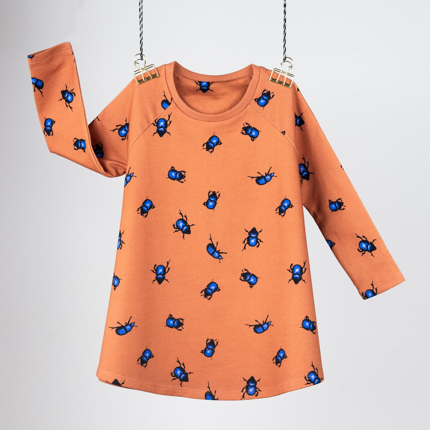 Front view of the Beetle's collection tunic dress. Hanging in front of a grey background. They are orange with blue beetles.