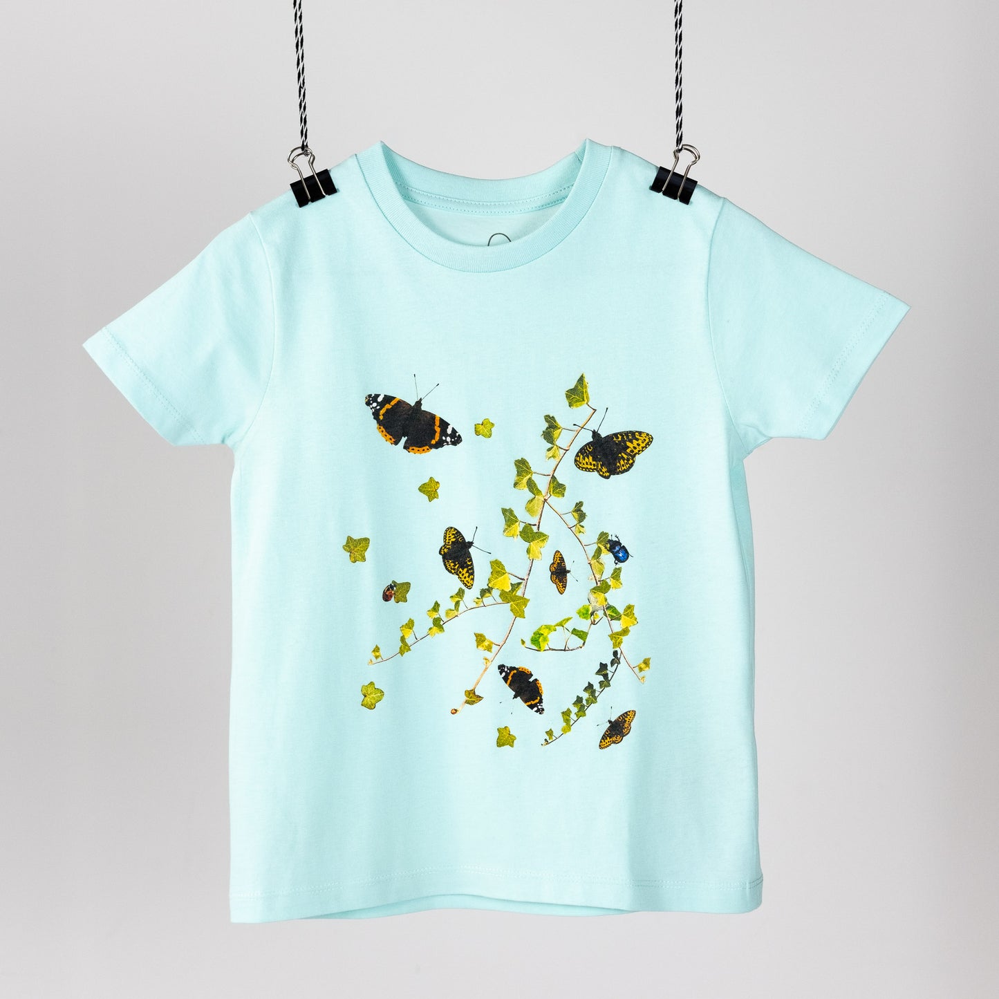 Green children's t-shirt with butterflies, ivy and other insects hanging like a piece of art. Front view 