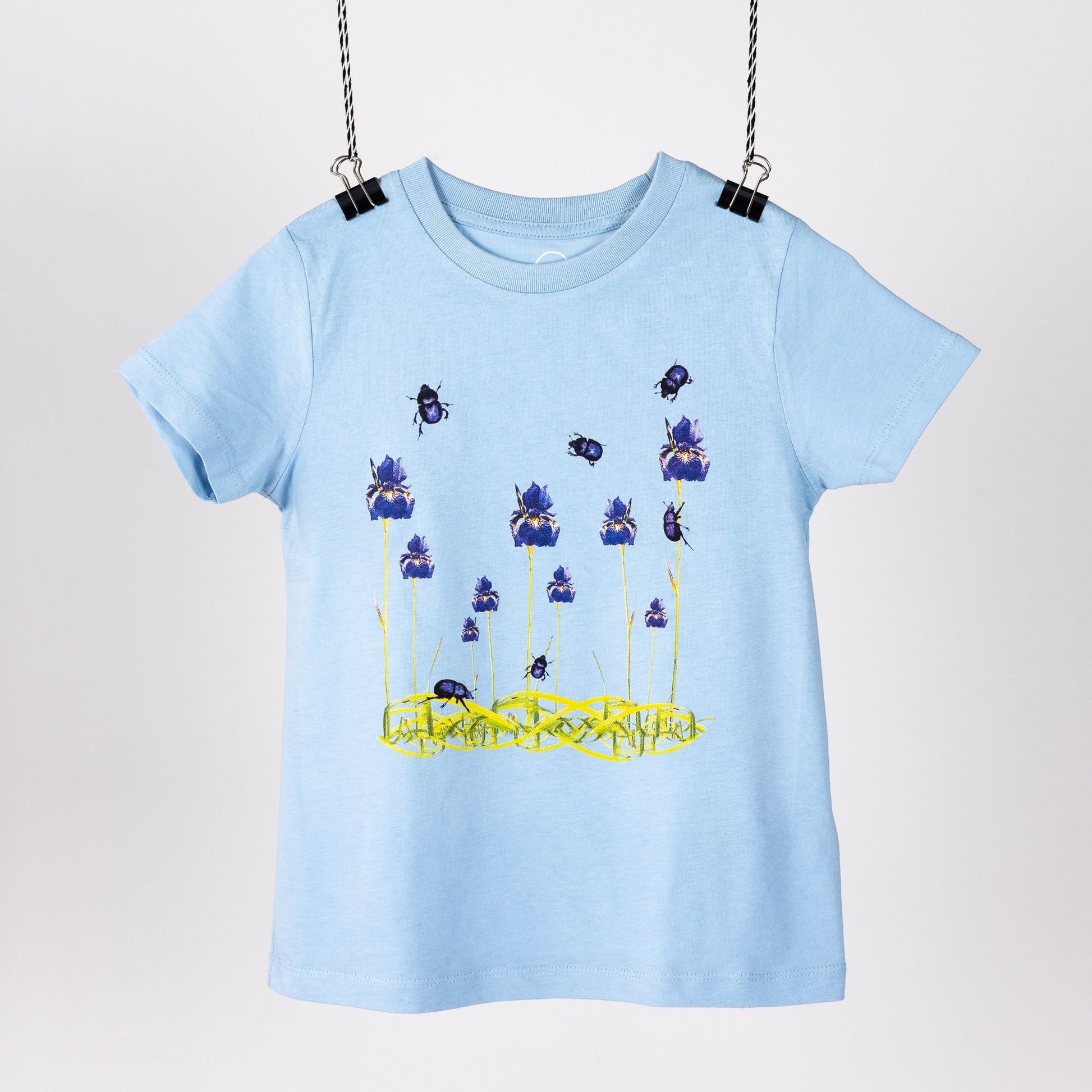 Light blue children's t-shirt with a digital print of blue irises and beetles. Hanging like a piece on art. Front view.