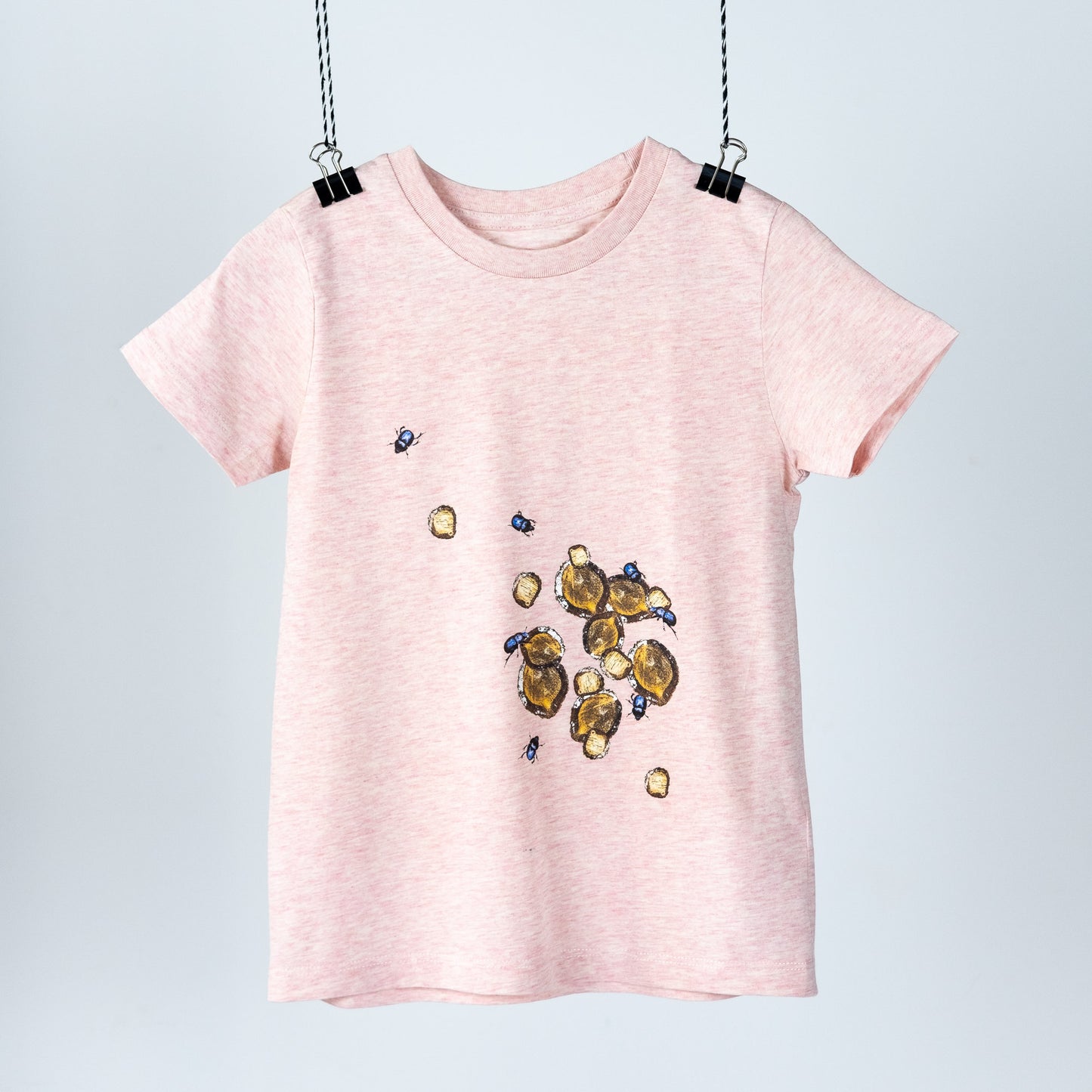 Heather pink children's t-shirt with logs and beetles hanging like a piece of art. Front view  